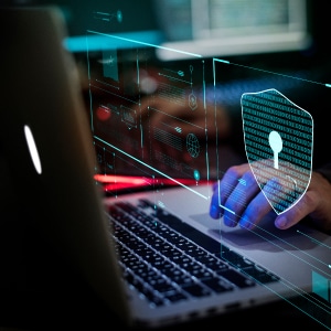 A person typing on a laptop with a security shield on it.